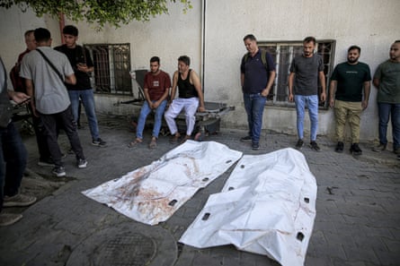 People stand near bodies covered with white sheets
