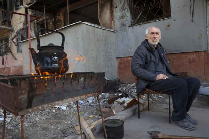 A man sits in front of an apartment building damaged from heavy fighting as he waits for the kettle to boil in an area controlled by Russian-backed separatist forces in Mariupol, Ukraine.