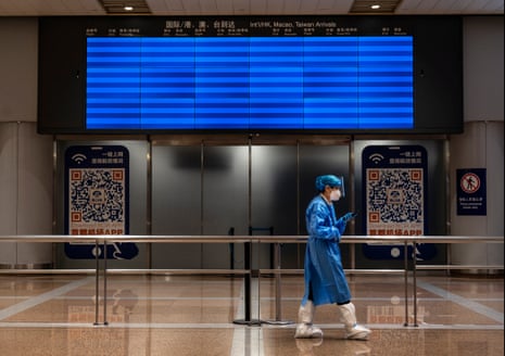A worker wearing PPE walks by an empty screen displaying no international flights in the international arrivals area of Beijing capital airport