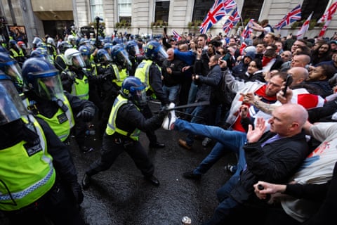 A line of riot police face a line of union jack-waving blokes, with one jeans leg kicking out towards a cop thrusting his baton.