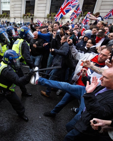 A line of riot police face a line of union jack-waving blokes, with one jeans leg kicking out towards a cop thrusting his baton.