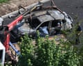 Aerial view of investigators examining a severely burned-out car being lifted by a red crane