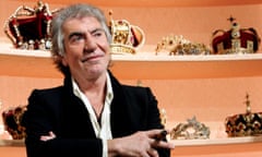 Roberto Cavalli with a cigar standing in front of two shelves full of crowns