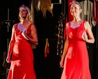 Two dancers in long red dresses on a stage made to look like a dressing room