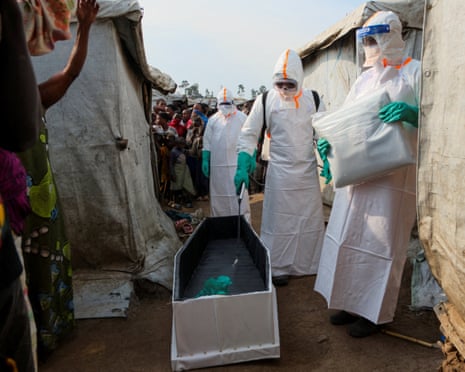 People in full PPE disinfect a simple wooden coffin laid out between densely packed tented accommodation.