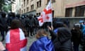 Demonstrators, one holding a Georgian flag, approach a line of riot police
