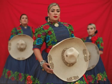 Three women in traditional dress hold on to their hats and look at the camera