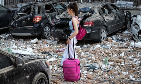 A girl with a suitcase stands next to cars damaged or wrecked by the rubble of a residential building hit by a downed kamikaze drone on 30 May 2023 in Kyiv, Ukraine.