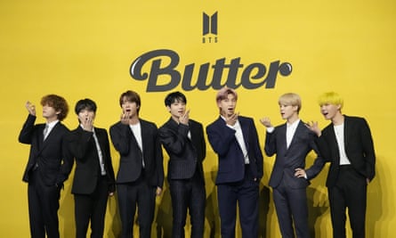 The boyband pose in dark suits and white shirts in front of a yellow backdrop reading ‘butter’