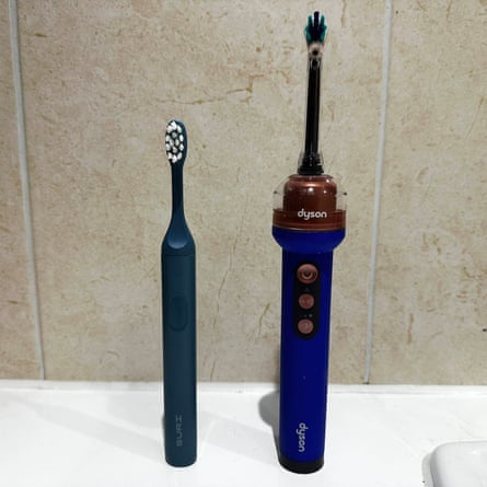 A compact Suri toothbrush stands beside a larger Dyson toothbrush with a bronze cap