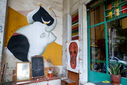 A painting of a black and white bull on a wall outside the cafe by the green framed window. A menu board stands in front of it.