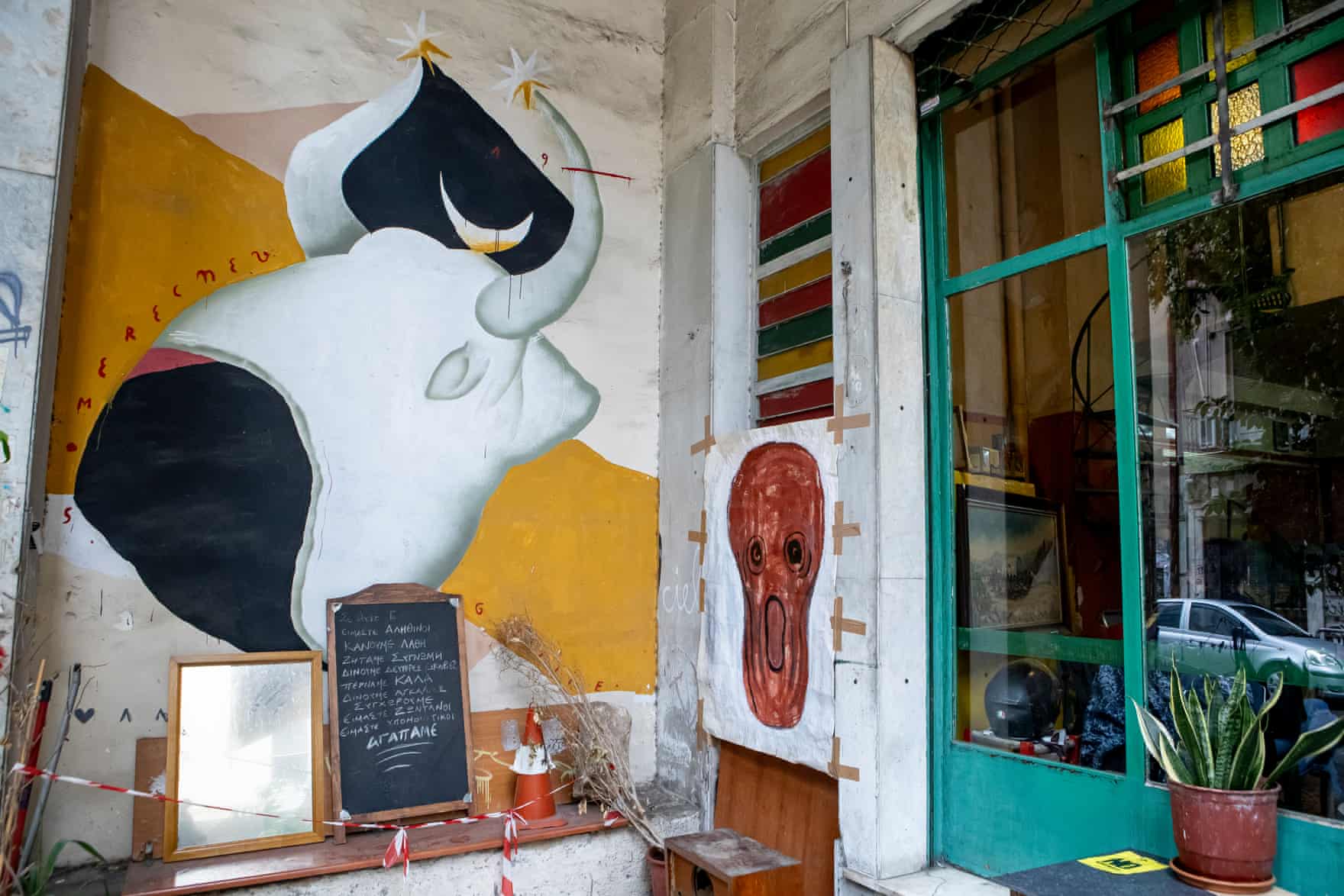 A painting of a black and white bull on a wall outside the cafe by the green framed window. A menu board stands in front of it.