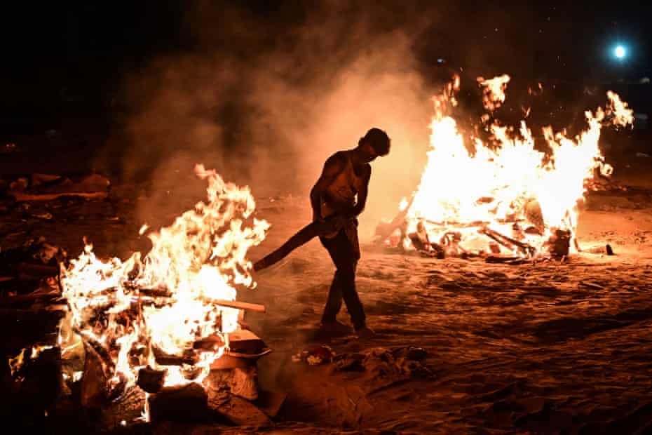 A worker helps cremate bodies on the banks of the river
