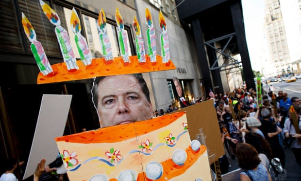 Fired FBI director James Comey emerges from a cake during a protest held on Trump’s birthday.
