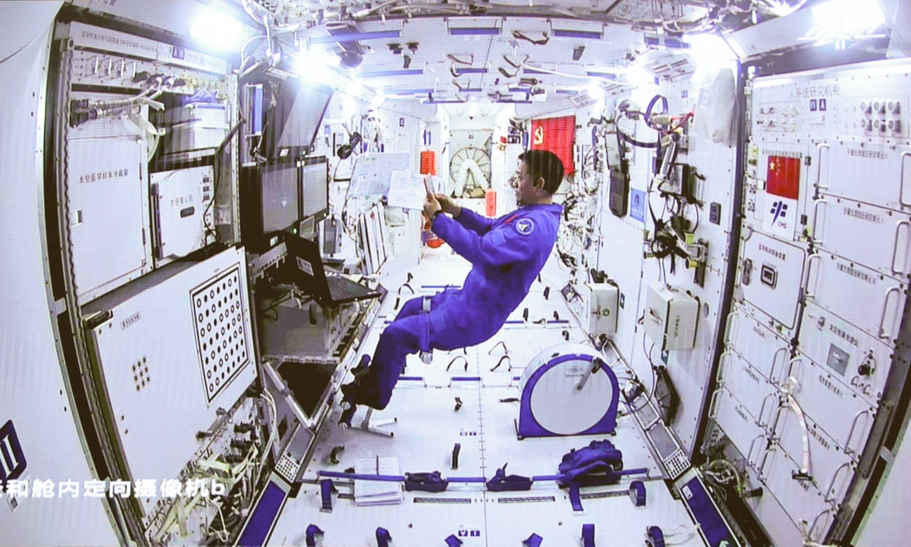 A man in a blue suit floats inside a space station module