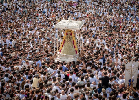 A colourful statue of the Virgin Mary is carried by a large crowd