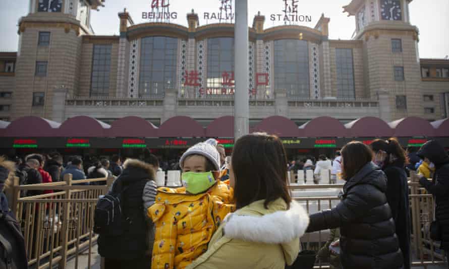 A woman holds a child wearing a face mask outside the Beijing Railway Station on Tuesday.