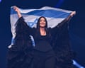 Yuval Raphael smiles holding an Israeli flag behind her head on stage