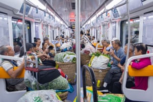 People sit in a metro-train carriage with large wicker baskets of fruit and vegetables in front of them