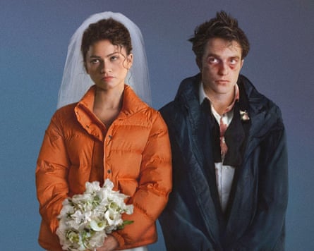 Zendaya in a veil and orange puffer jacket stands beside a bruised Robert Pattinson in a coat