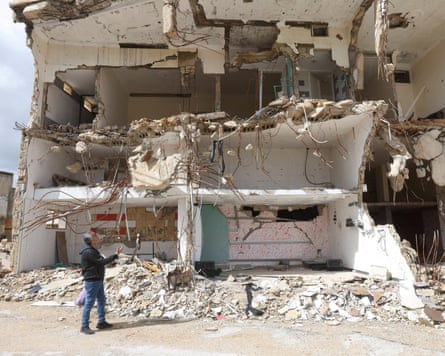 A man stands beside the remains of a three-storey building missing its front wall