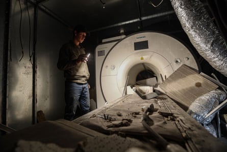 A man shines a torch on an MRI scanner covered in debris.