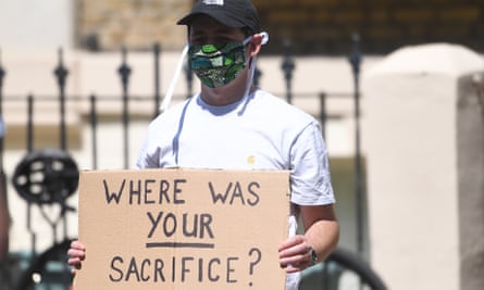 A masked protester outside Dominic Cummings’s home holding a placard saying 'Where was your sacrifice?'