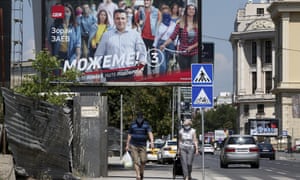 A couple wearing face masks to protect against coronavirus, walk under an electoral poster of the leader of the ruling Social Democrats Zoran Zaev, in a street in Skopje, North Macedonia on Saturday,