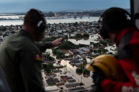 Two people look out of a helicopter at flooded houses