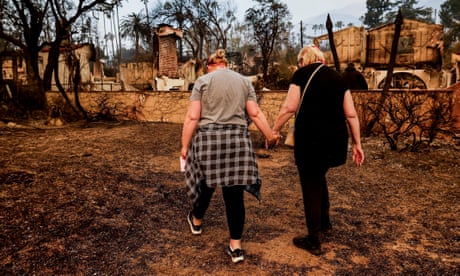 a mother and daughter hold hands near their burned home