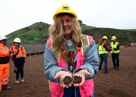 woman wearing pink safety vest and hard hat holds soil in hands