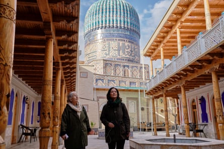 Mishal Husain and her mother, Shama, walking between buildings with wooden balconies, with a richly decorated blue dome in the background, in Samarkand 