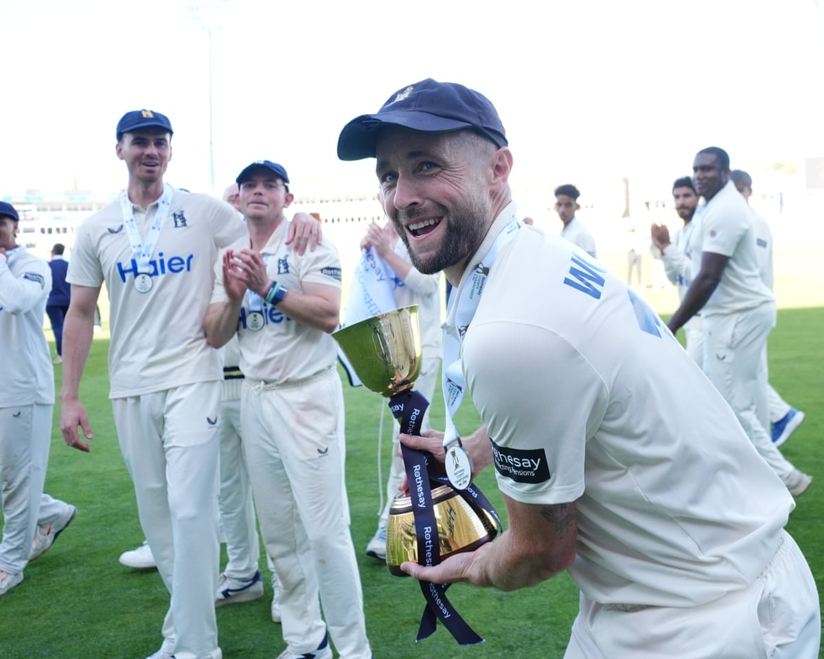 The Warwickshire cricketer Chris Woakes, leading a group of his teammates towards the stands, celebrates with the County Championship trophy.