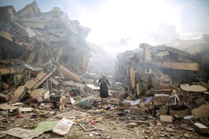 A resident of al-Zahra walks through the rubble of homes destroyed in Israeli airstrikes in Gaza City as smoke appears to linger.