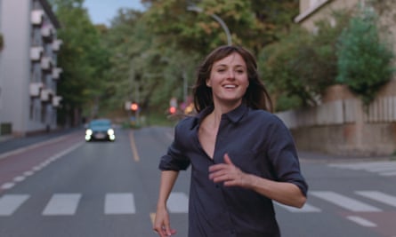 Renate Reinsve running down the middle of an urban street grinning.