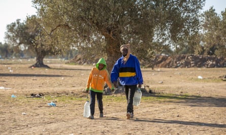 A man and a young boy carrying large water bottles in Sfax.