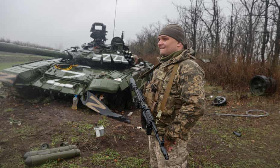 A Ukrainian service member stands next to a damaged Russian tank