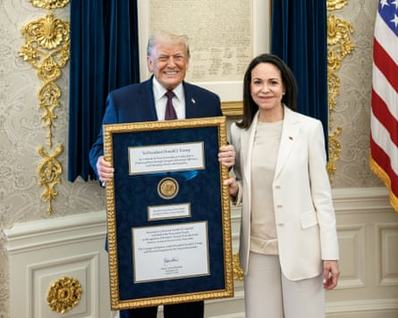 Machado stands next to Trump, who grins as he holds up a large gilded frame containing a gold medal