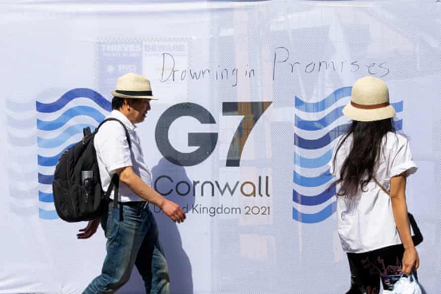 People walk past a sign saying 'Drowning in Promises' written near the media centre in Falmouth