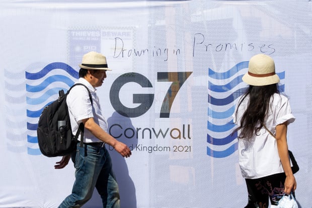 People walk past a sign saying ‘Drowning in Promises’ written near the media centre in Falmouth