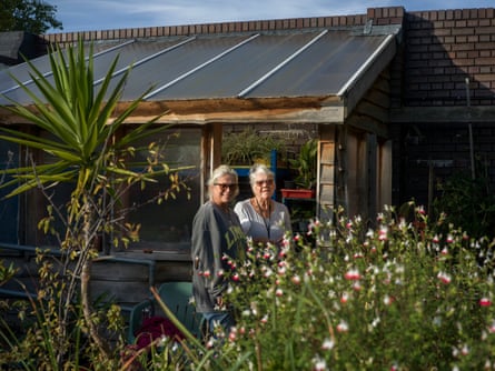 A middle-aged woman and an older woman stand by a building behind a flower bed