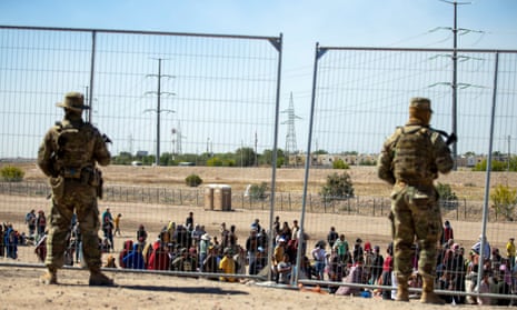 Migrants wait in line adjacent to the border fence under the watch of the Texas national guard to enter into El Paso, Texas, on 10 May.