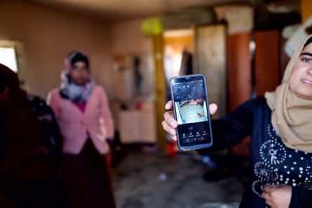 A woman holds an image on a phone up to the camera 