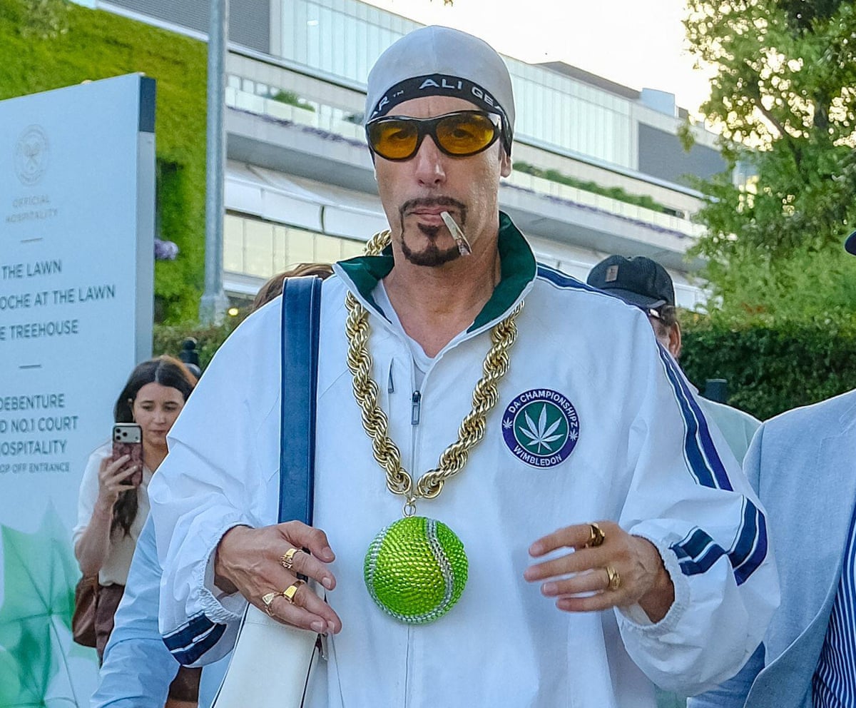 Sacha Baron Cohen in character as Ali G, wearing, sunglasses and a white tracksuit top with Wimbledon logo and a giant green tennis ball on a chunky gold chain round his neck