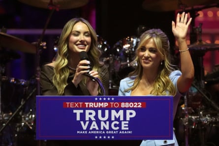 Two women smile while standing at a lectern with a ‘Trump Vance’ sign