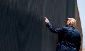 a man in a suit points to a fence along a border