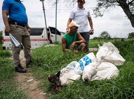 Two dogs breathe through holes cut into canvas sacks as a trader kneels before the local police chief on the side of a road