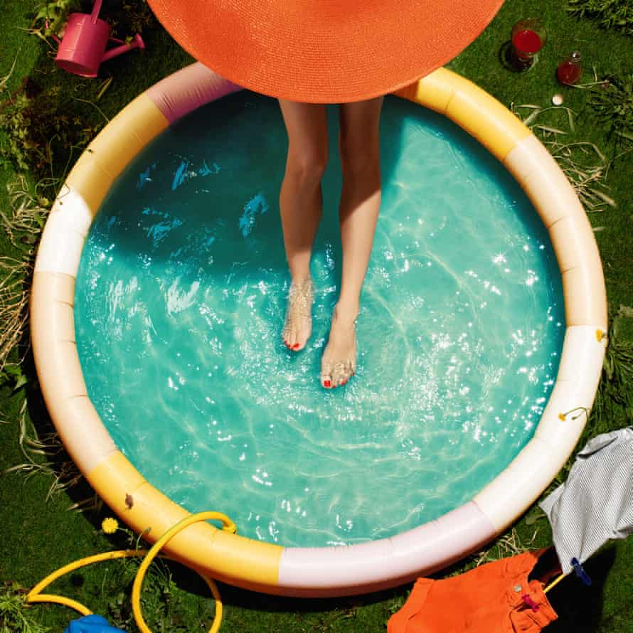 An overhead shot of a woman wearing a big hat with her feet in a paddling pool