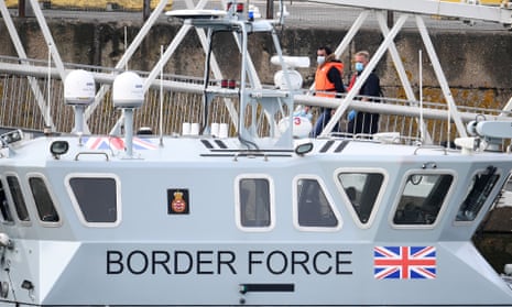 A UK Border Force staff walks a migrant up a ramp past a Border Force vessel in Dover