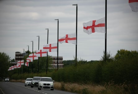 A line of red and white England flags attached to lamp-posts on a road near Birmingham as cars drive past.